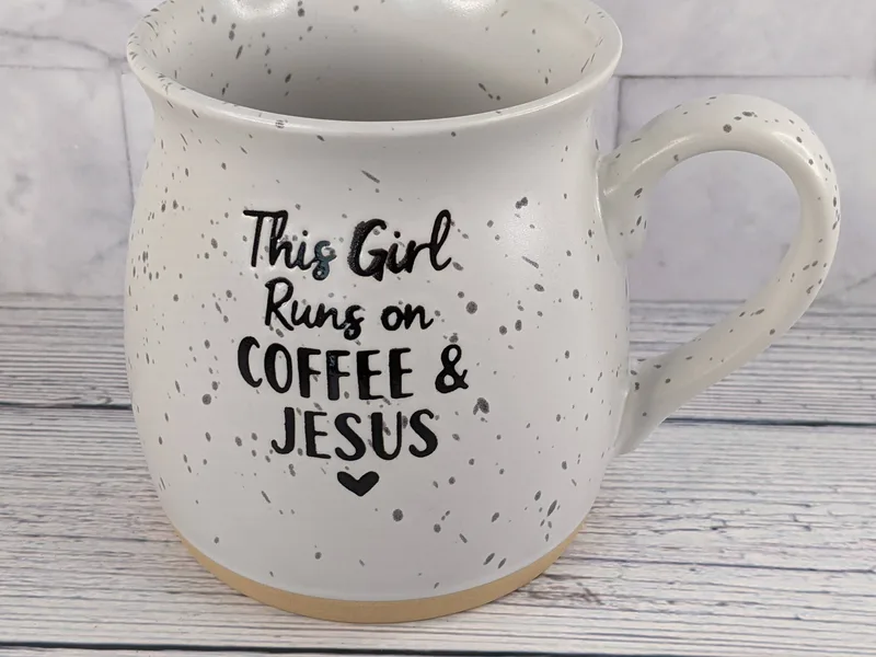 A stoneware mug with the words, "This girl runs on coffee and Jesus."