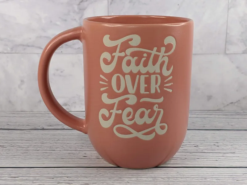 A coral-colored mug with the words "Faith over fear."