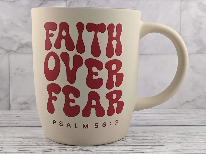A tan mug with red lettering that says, "Faith over fear. Psalm 56:3"