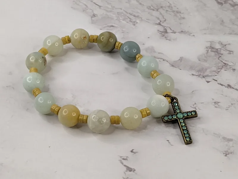 A beaded stretch bracelet with gold and blue amazonite beads and a metal cross charm with an inlay of turquoise stones.
