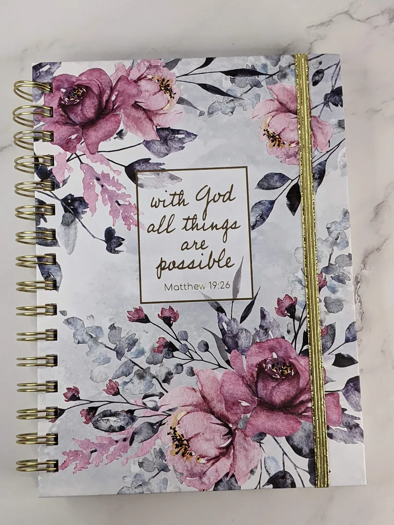 A religious spiral journal with a Bible verse on the cover, "with God all things are possible," and a purple flower design.