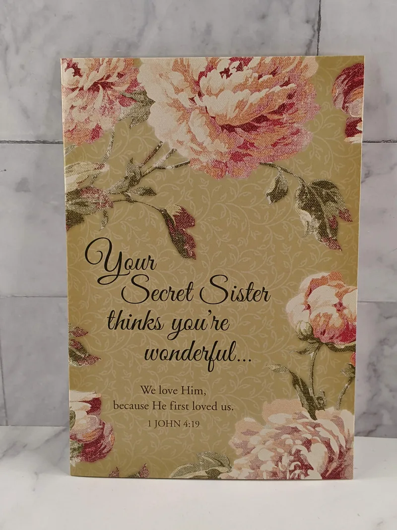 A Secret Sister greeting card with a tan cover, pink flower design, and a thinking-of-you message.