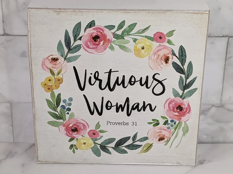 A white wooden sign with a pink floral design, featuring the words "Virtuous Woman - Proverbs 31"