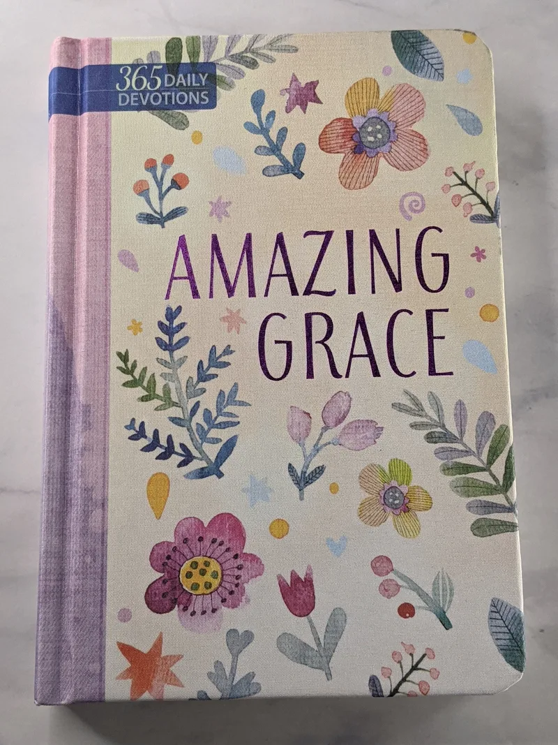 A religious book of devotions with a purple spine, floral design on the cover, and a theme of Amazing Grace.