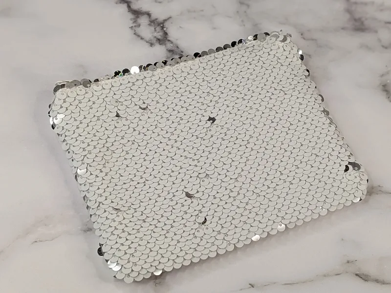 A small-zippered pouch covered in white sequins that are silver when their direction is reversed.