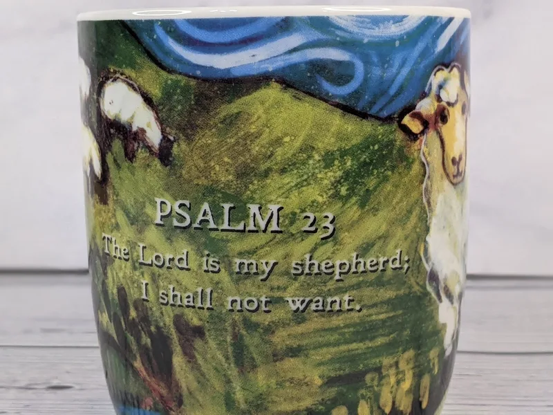 A Christian mug with sheep artwork in vivid colors, featuring a Psalm 23 Bible verse.