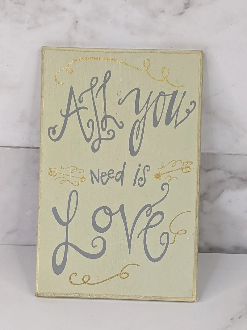 A rectangular cream-colored magnet with the words "all you need is love" in silver lettering.