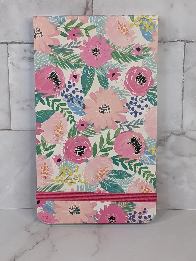 This pink flower designed flip notebook has lined pages with a floral design, and a pink elastic closure. 