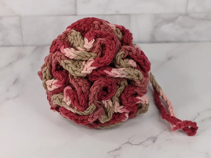 A crocheted bath sponge loofa in pink shades, made of cotton yarn.