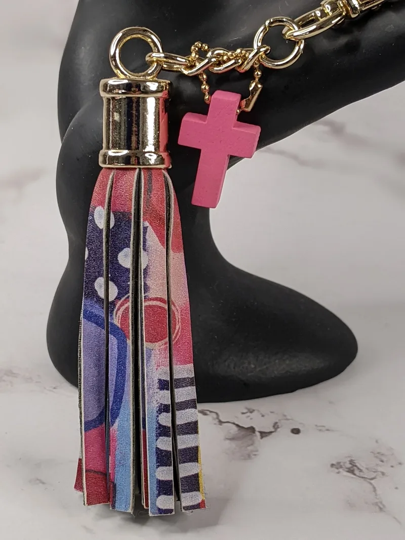This cute colorful leather-like tassel keyring has a pink cross charm and a gold key clip. 