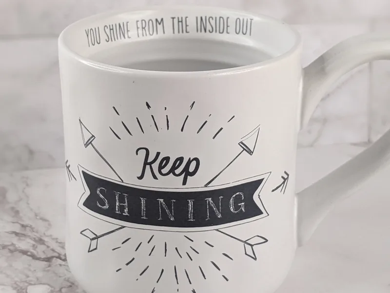 A white Scripture mug with a "Light of the World" verse, and the words "Keep Shining" in black letters.