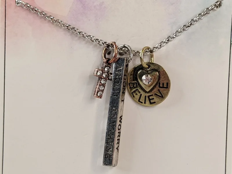 A religious silver necklace chain with three charm pendants featuring a cross and the words, "don't worry, instead pray."