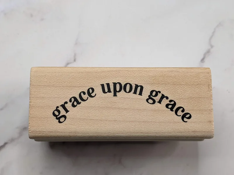 A rubber stamp mounted on a wooden block that says, "grace upon grace."