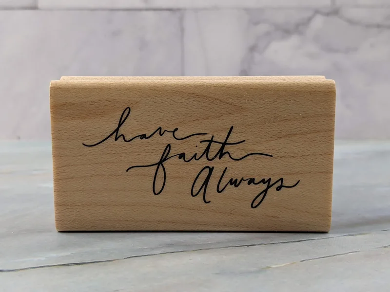 A rubber stamp mounted on a wooden block that says, "Have faith always."
