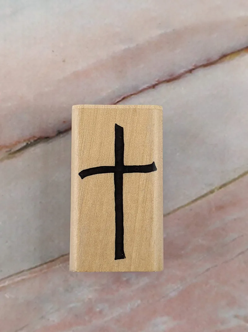 A rubber stamp with an image of a cross, mounted on a wooden block.