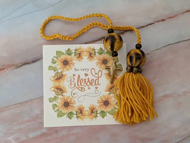 A yellow yarn bookmark with a tag that has the words "so very blessed" and a sunflower design.