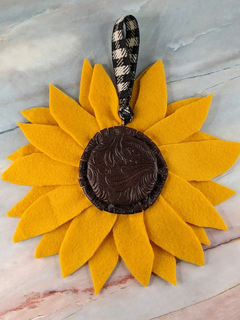 A yellow fabric handmade sunflower with a brown faux leather center and a black & white gingham ribbon.