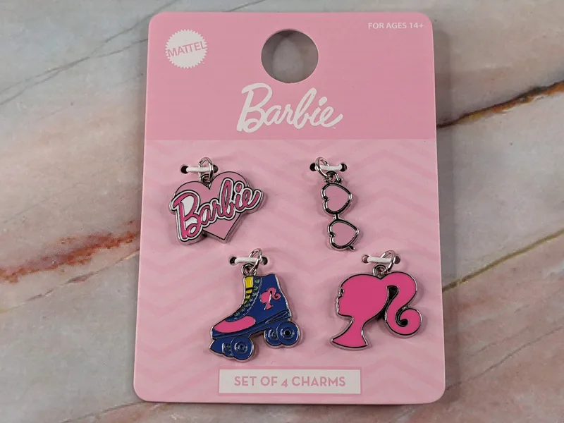 A set of 4 Barbie metal jewelry charms: a pink Barbie logo, heart sunglasses, roller skate, and a Barbie silhouette.