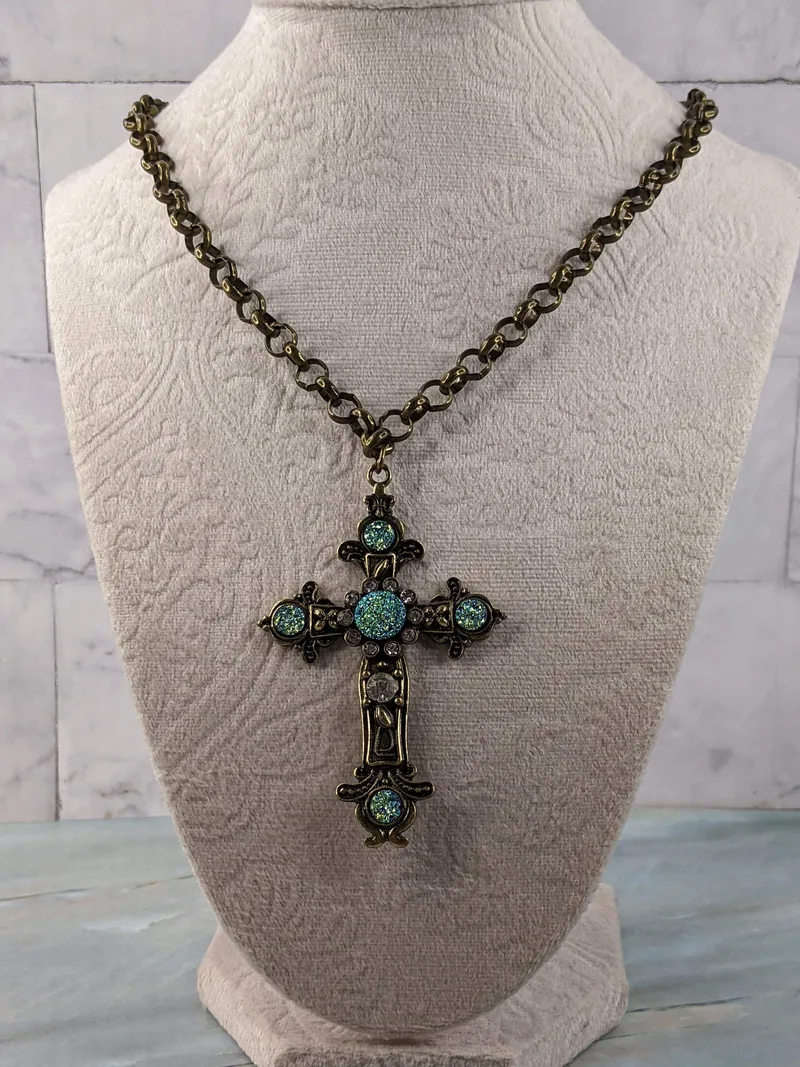 A long gold chain necklace with a metal cross pendant that has blue and clear rhinestones.