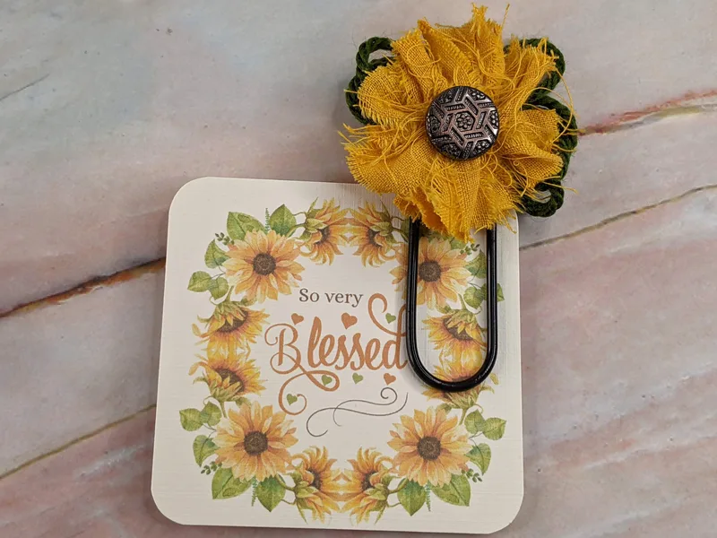A "so very blessed" tag with a jumbo black paperclip attached with a handmade fabric sunflower.