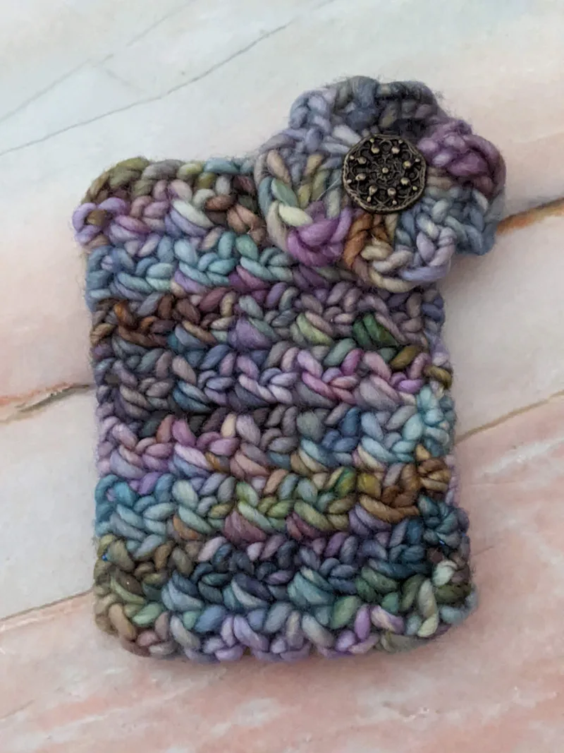A crocheted yarn gift card holder bag that's blue and purple with a crocheted flower.
