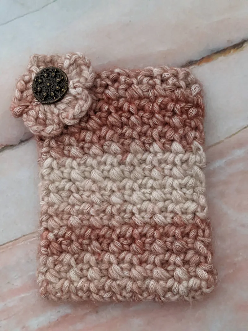 A crocheted gift card holder with a flower motif in neutral tan tones.
