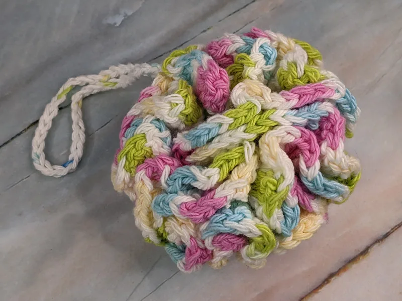A crocheted bath scrubber with a loop handle, made with colorful cotton yarn.