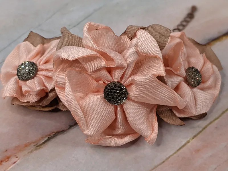A dark gold chain bracelet with three pink fabric handmade flowers with taupe fabric leaves.