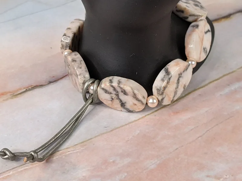 A beautiful stretch bracelet with pink and gray natural zebra stone beads, small glass pearls, and a leather cord decoration.
