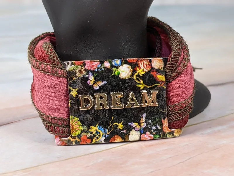 This gorgeous rosy pink cloth wrap bracelet, with a black "dream" tag with a floral design, wraps around the wrist.