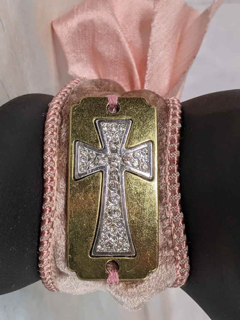 A rose velvet cuff bracelet with a pink silk ribbon bow and a gold metal cross tag.