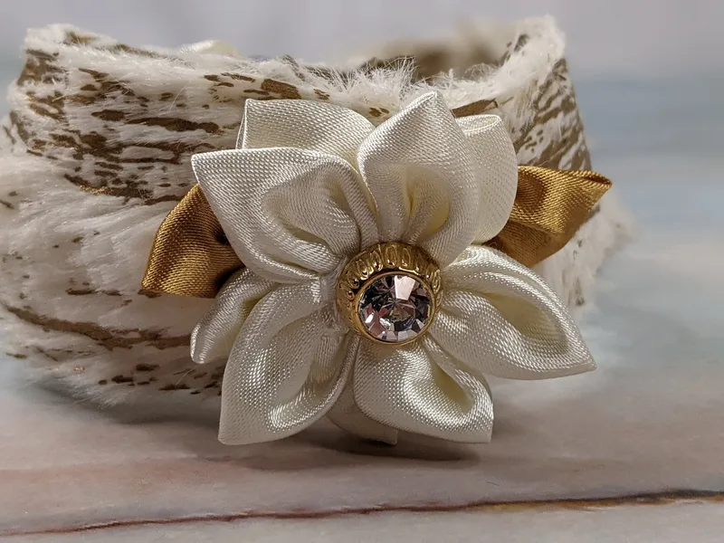 A cream and gold faux fur fabric cuff bracelet with a satin ribbon bow and a satin cream handmade flower accent.