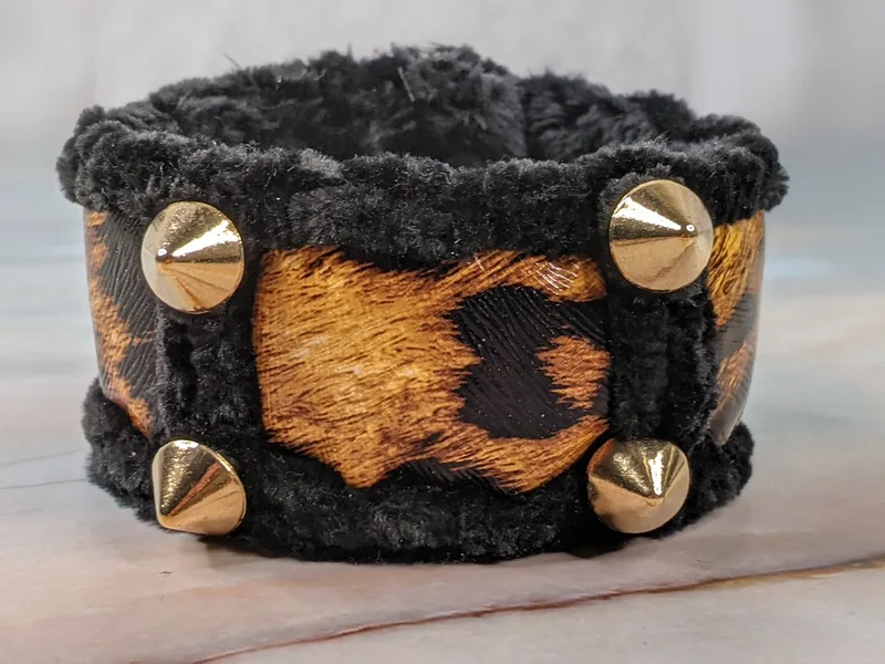 A faux leather cuff bracelet with a brown and black leopard print band, gold metal spikes and a black fur lining.