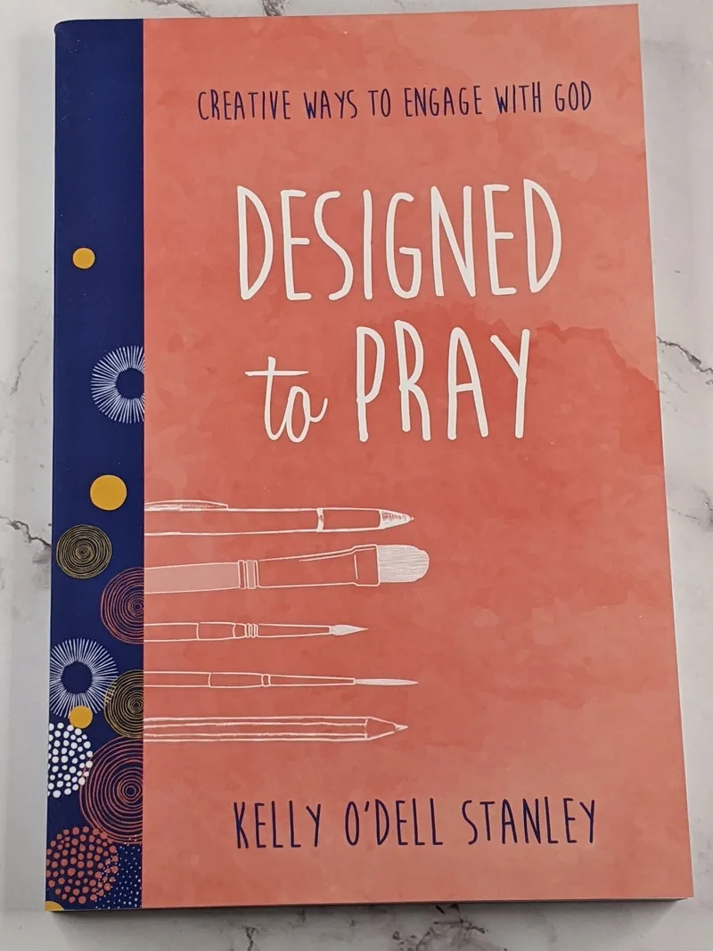 A book with an orangish red cover and the title, Designed to Pray.
