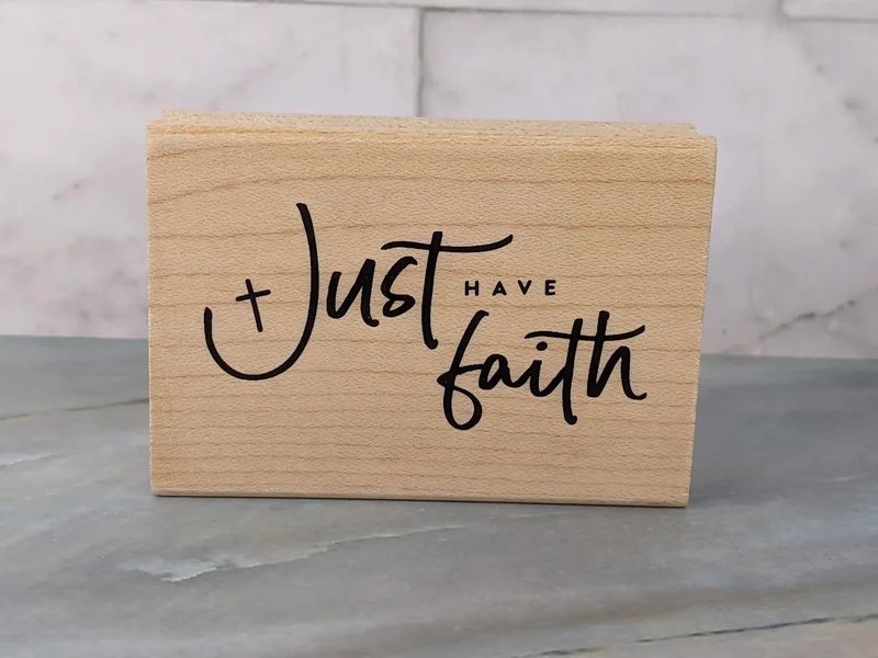 A rubber stamp mounted on a wooden block that says, "Just have faith."