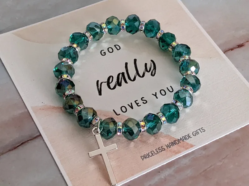  A beautiful stretch bracelet with teal glass beads, a metal cross charm, and a "God really loves you" paper tag.