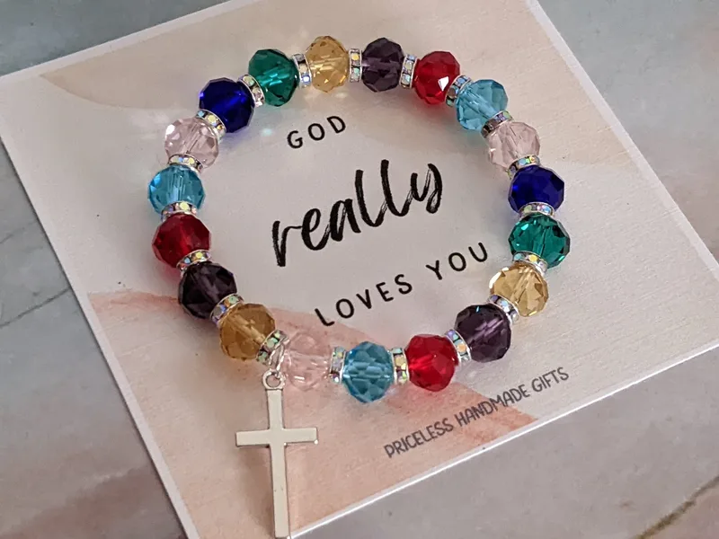 A beautiful stretch bracelet with multi-color faceted glass beads, a metal cross charm, and a "God really loves you" paper tag.