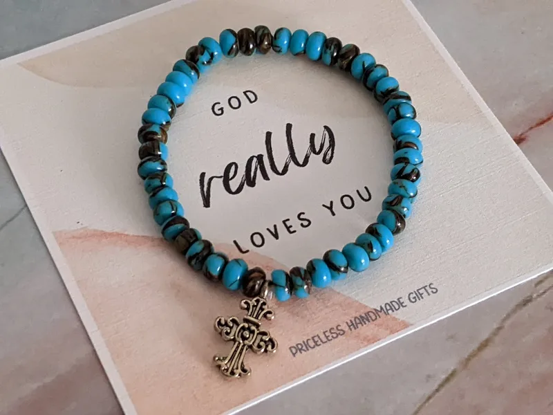  A beautiful stretch bracelet with turquoise/brown reconstituted siderolite stone beads, a metal cross charm, and a "God really loves you" paper tag.