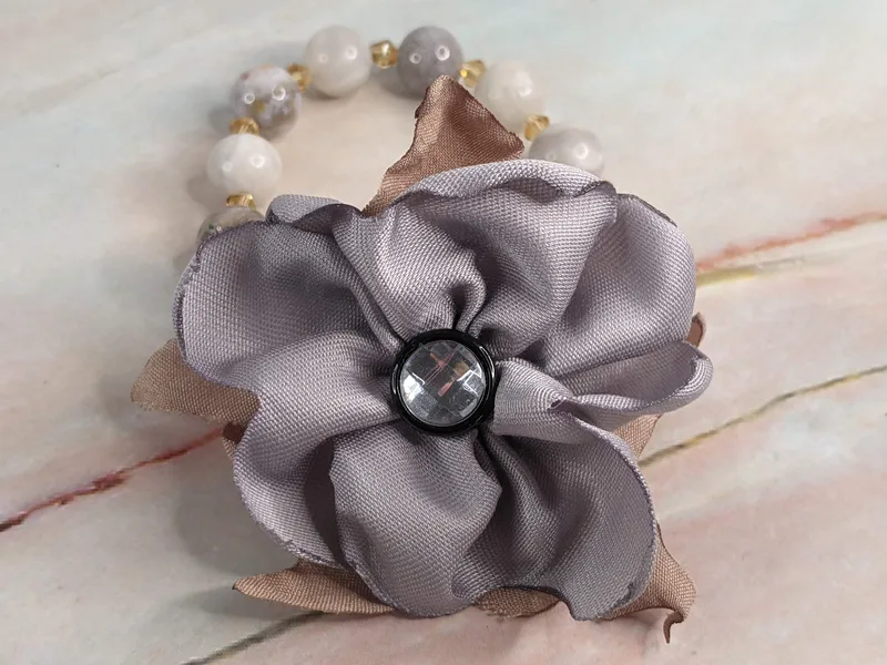 A stretch bracelet made with natural agate stone beads in browns and grays, golden crystal spacer beads, a gray handmade flower with a gem button center.