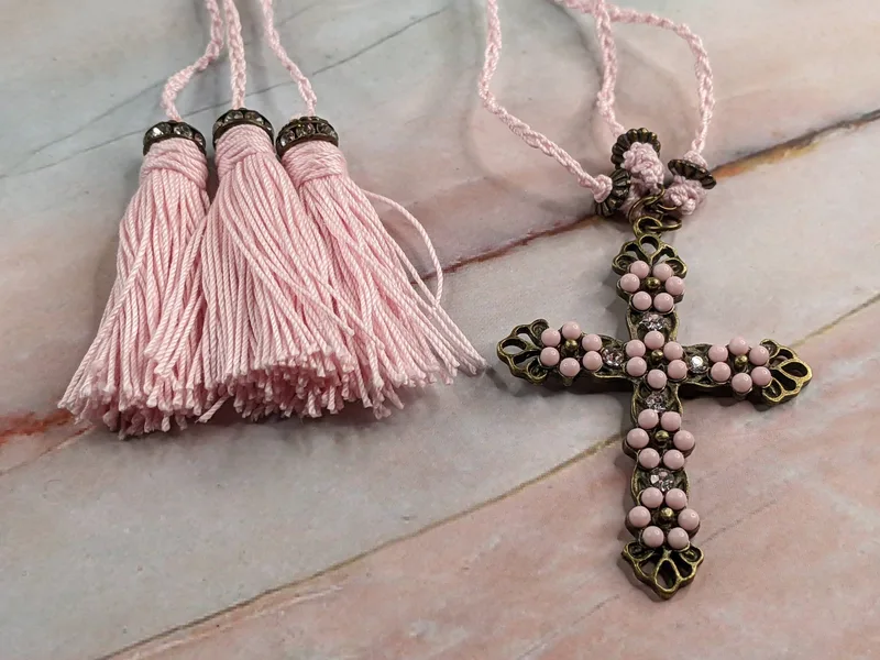  A pink and gold crocheted bookmark with three strands, three pretty tassels, and a gorgeous cross pendant inset with pink stones and sparkly rhinestones.