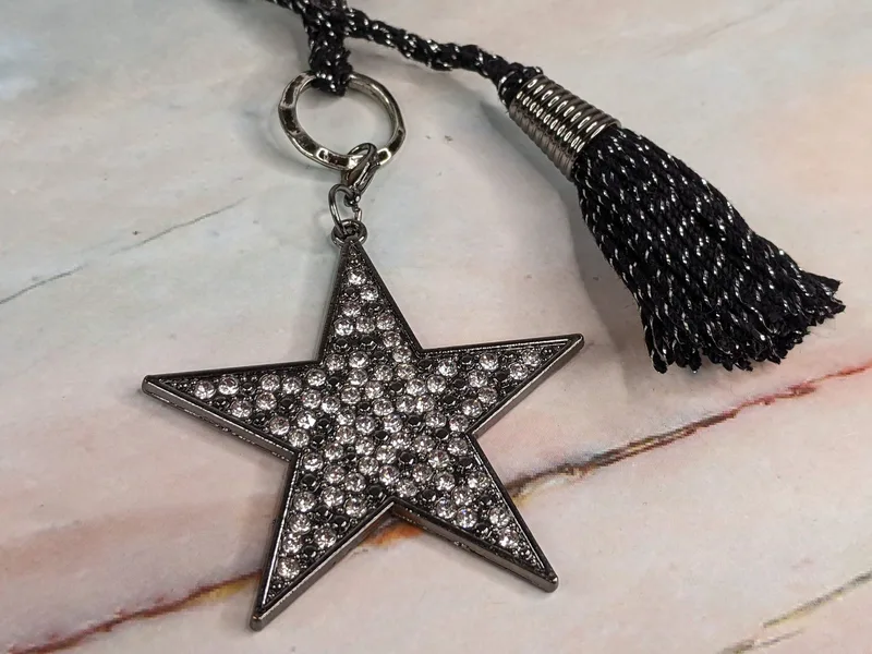 A black yarn bookmark with a large yarn tassel and a rhinestone star shaped pendant.