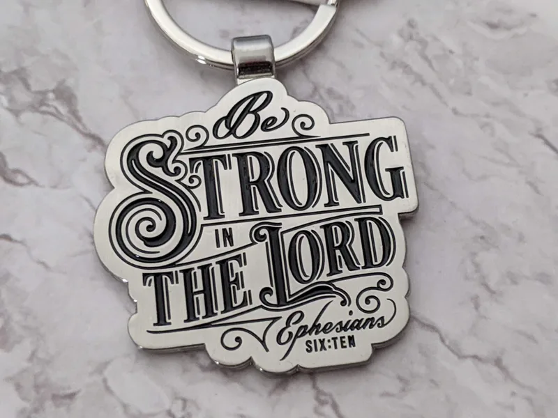 A metal scripture keyring with the Bible verse Ephesians 6:10: Be strong in the Lord and in His mighty power.