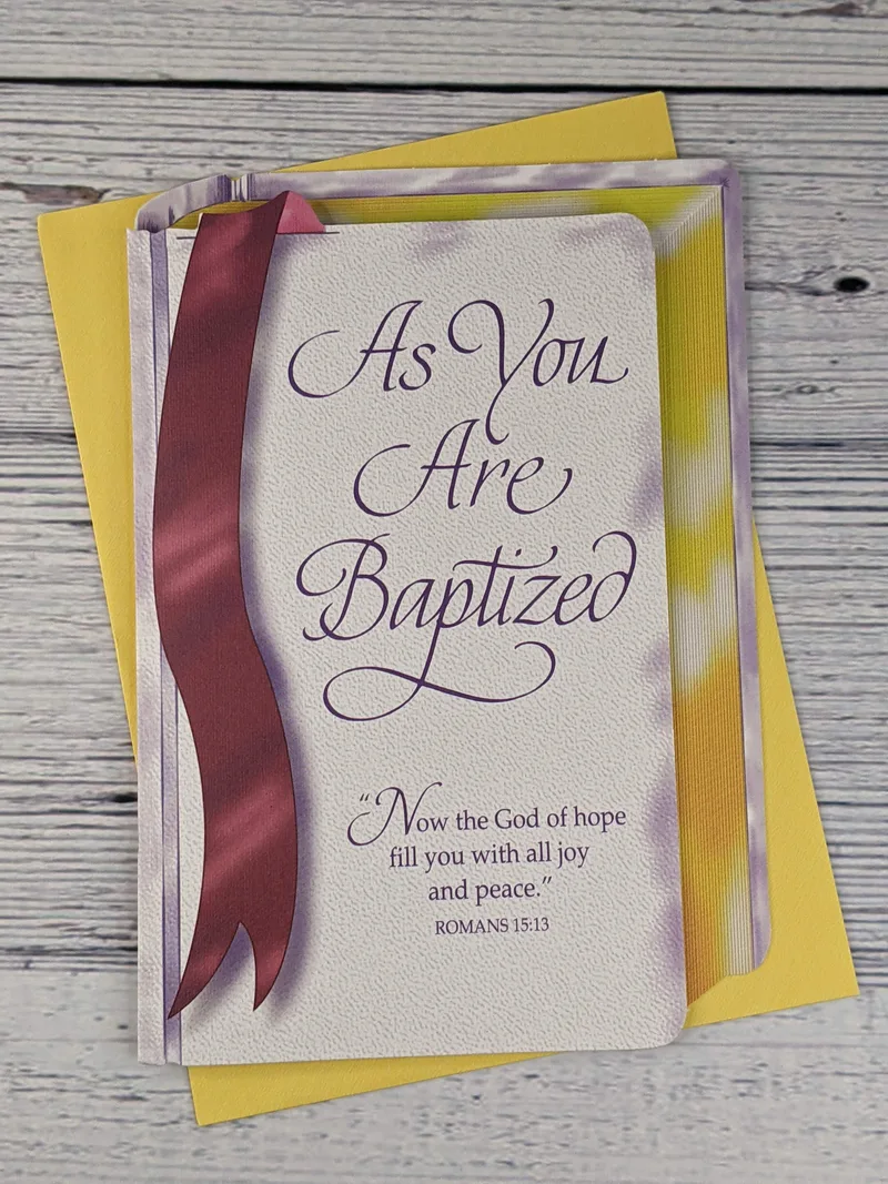 A Christian baptism card that is shaped like a Bible.