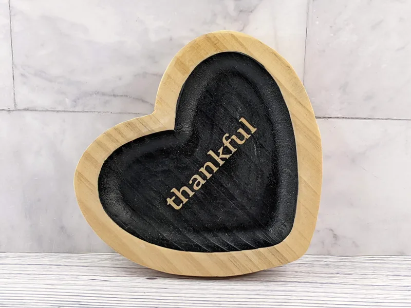 A heart shaped trinket tray made of wood with black paint and the word "thankful."