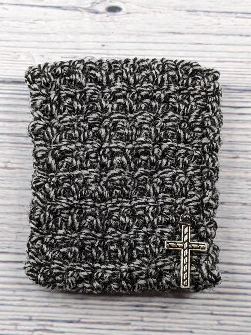 A crocheted black and gray gift card holder with a silver cross charm.