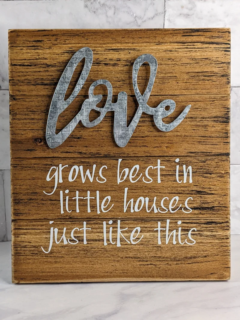 A rustic wooden plaque that has an inspirational message, "Love grows best in little houses just like this."