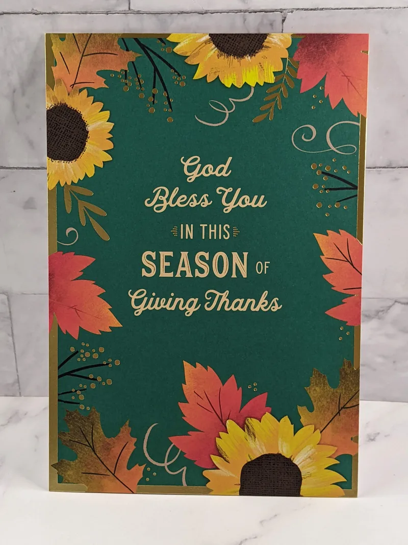 A teal cover on a greeting card with images of yellow sunflowers and red leaves.