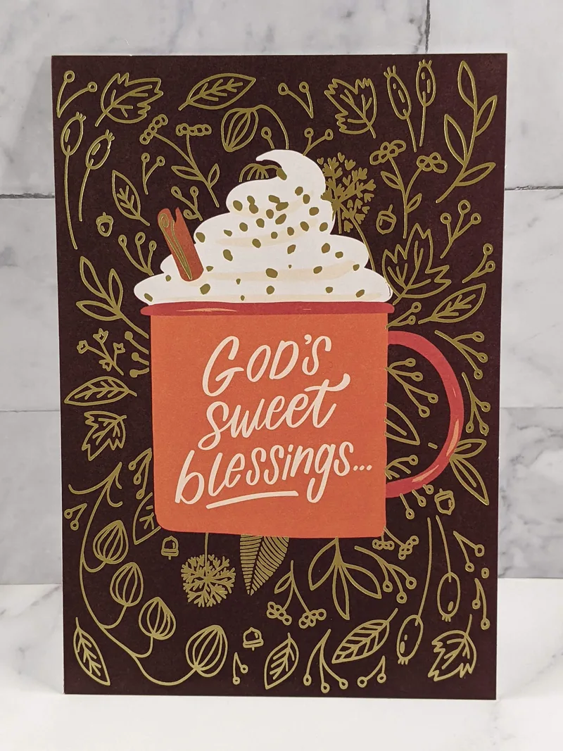 A Thanksgiving greeting card with a brown background, golden leaf design, and an image of a latte in an orange mug with the words "God's sweet blessings."