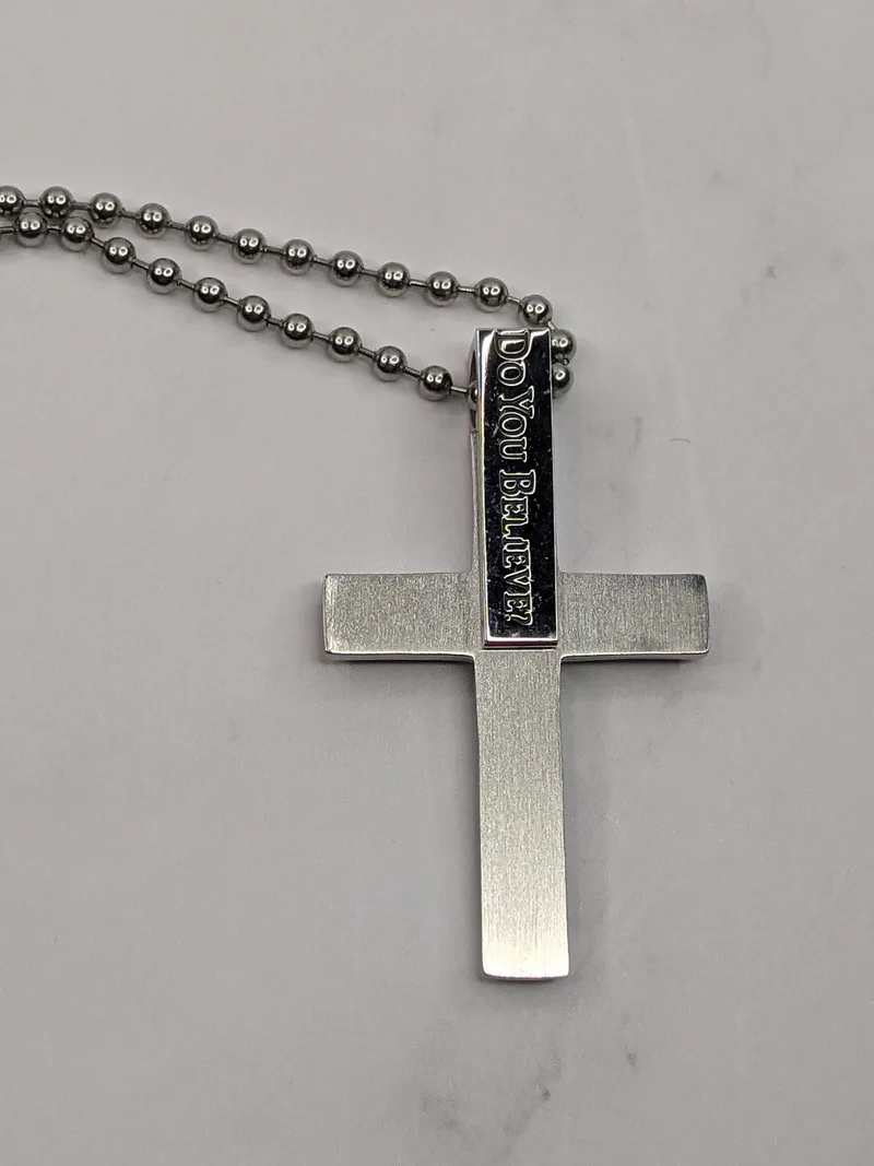 A silver chain necklace with a stainless-steel cross pendant that references a Bible verse.