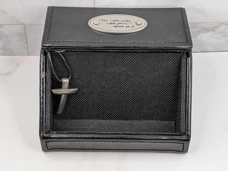 A black business card holder for a pastor with a Bible verse inscribed on a metal plate and a silver cross charm. 